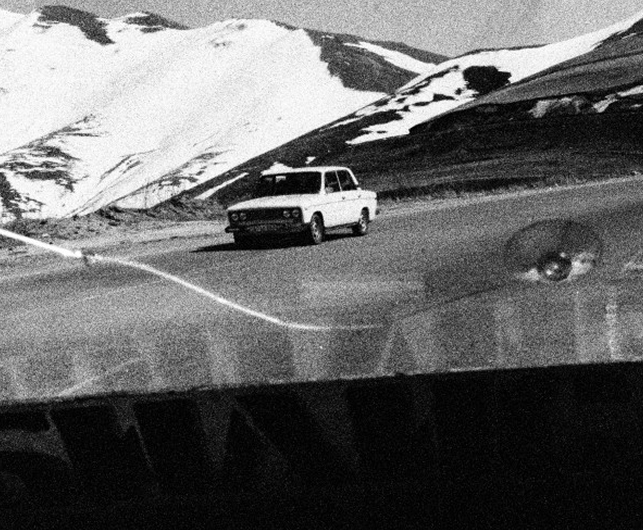 Vintage black and white photograph of a classic car driving along a mountain road, overlaid with an AI-generated title, description and keywords